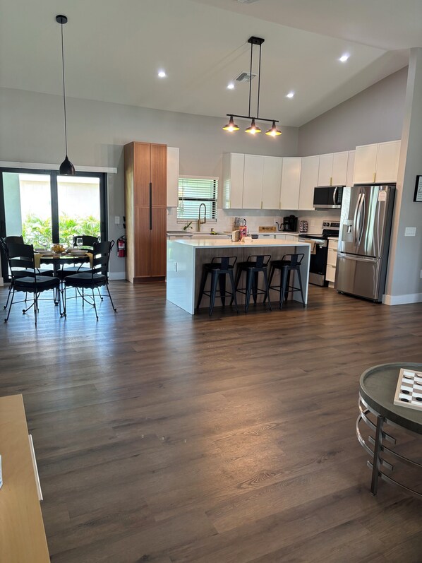 A modern kitchen with a central island, bar stools, and a dining area with a table and chairs.