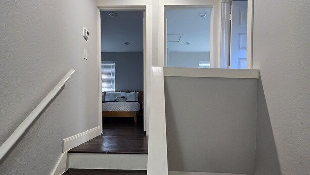 Eine Treppe mit weißen Geländern führt zu einem Schlafzimmer mit Bett und Fenster.