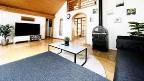 Un ampio soggiorno con soffitto in legno, televisore a schermo piatto, camino e una grande finestra.