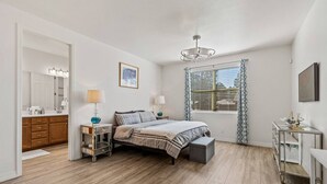 Un dormitorio con cama, mesitas de noche, escritorio, espejo y ventana con persianas.