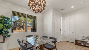 Un comedor moderno con una mesa de vidrio, cuatro sillas, una planta en maceta y un banco con un cojín que dice 'bienvenido a casa'.
