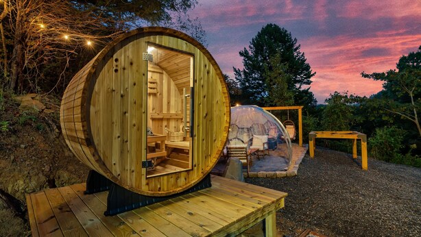 A wooden cabin with a circular interior, a transparent dome structure, and a wooden deck. - Lux Sauna, Dome, Stargazing Net, Putting Green (Sevierville)