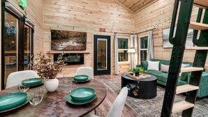 A wooden interior with a dining table set with green plates, a white vase with flowers, and a painting of a river scene. - Lux Sauna, Dome, Stargazing Net, Putting Green (Sevierville)