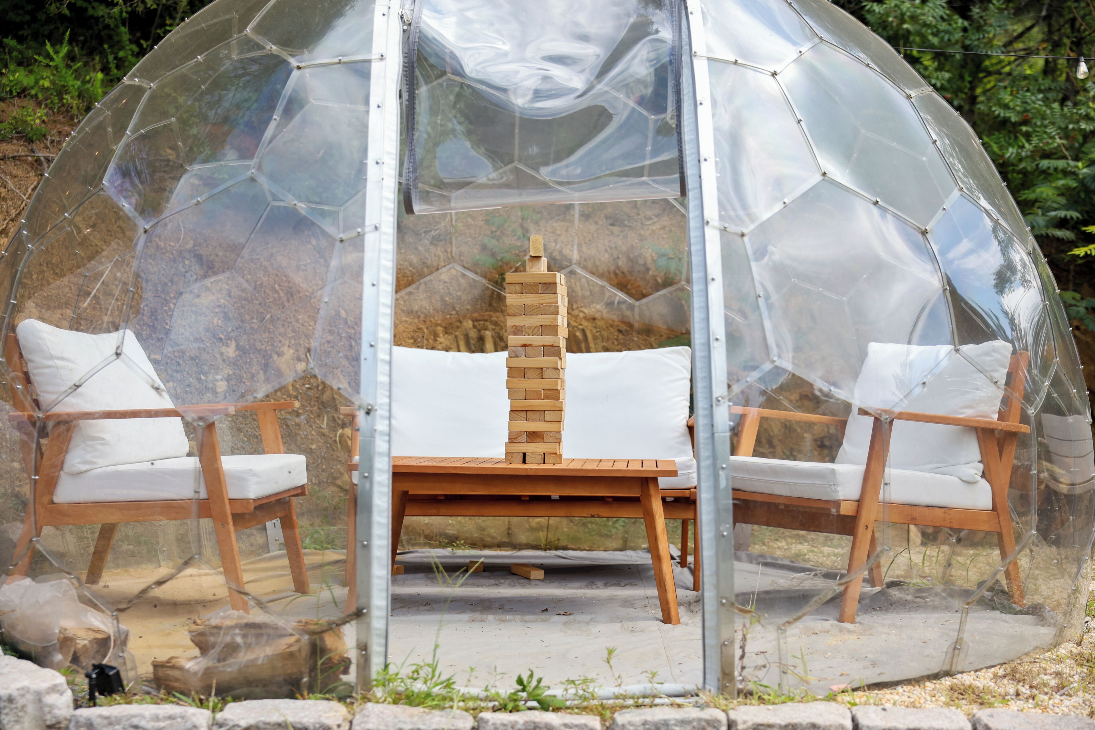 A transparent dome structure with two wooden chairs and a table inside.