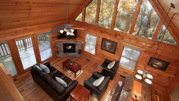 Une cabane spacieuse avec un intérieur en bois, une cheminée et de grandes fenêtres donnant sur la forêt.