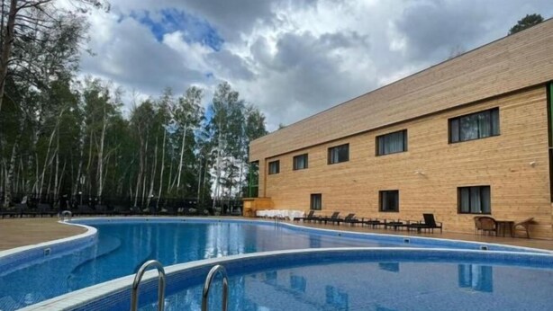 Una piscina con bordo in legno, un edificio con molte finestre e alberi sullo sfondo.