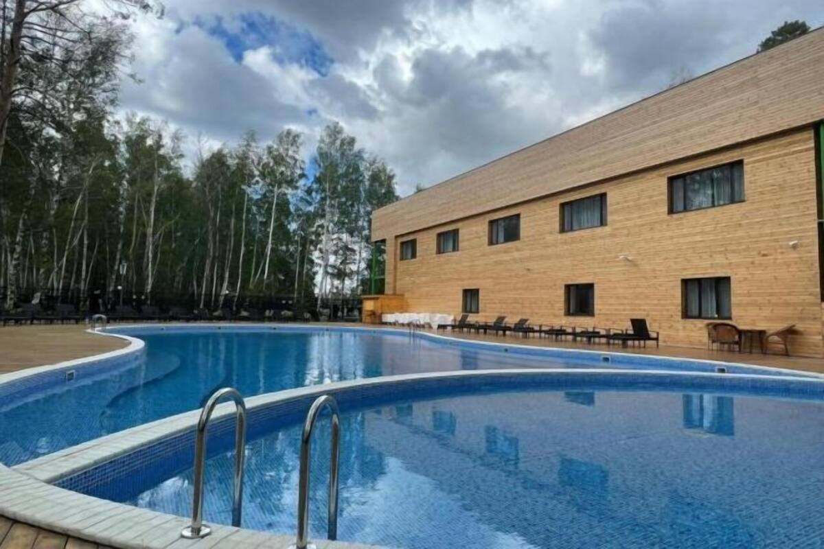 A swimming pool with a wooden deck, a building with multiple windows, and trees in the background.