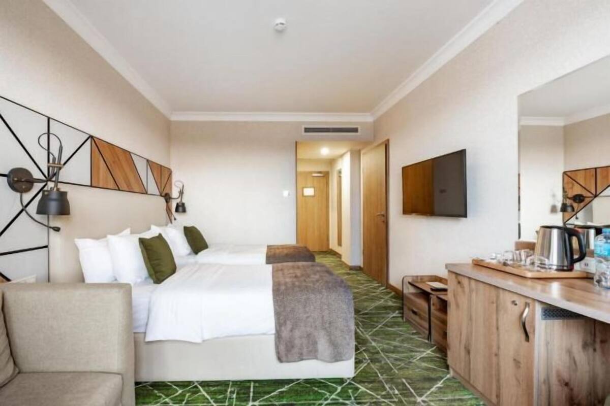 A hotel room with two beds, a kitchenette, a TV, and a mirror.