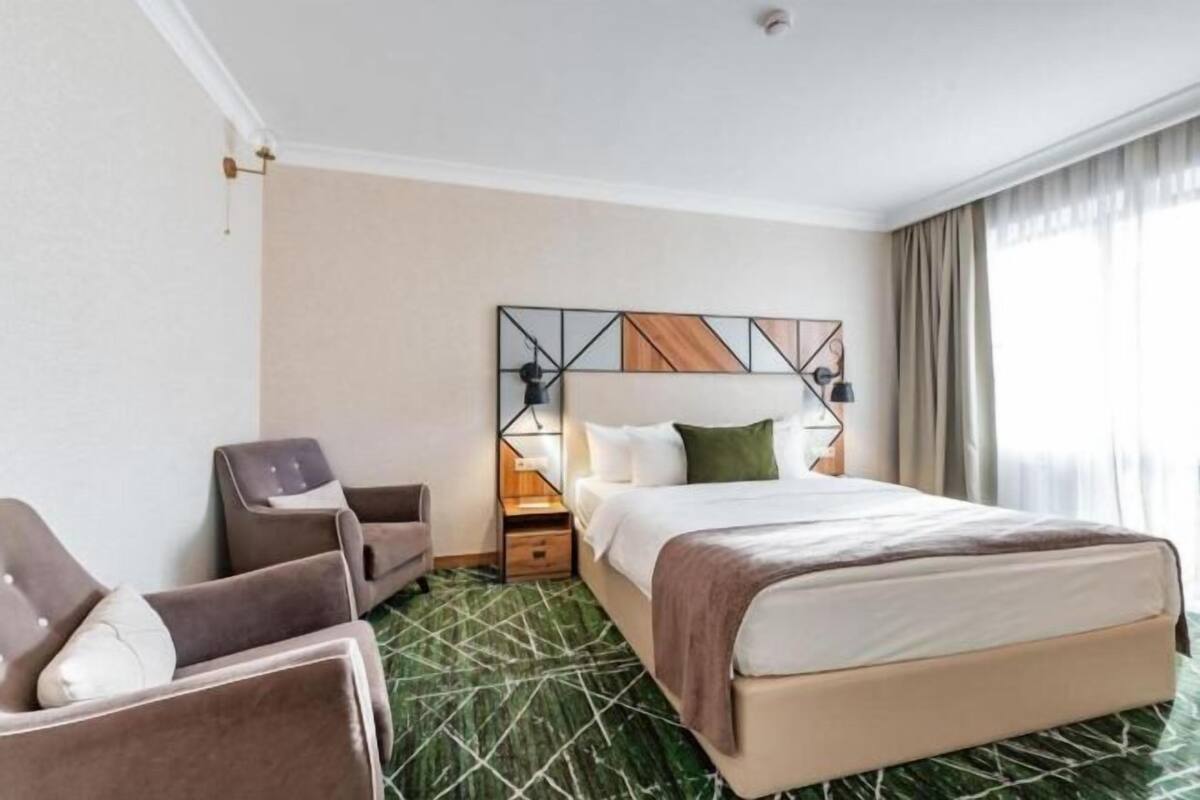 A hotel room with a bed, a chair, a nightstand, and a lamp.