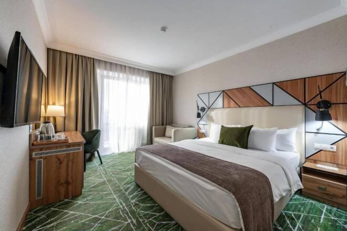 A hotel room with a bed, a desk, a chair, a TV, and a large window with curtains.