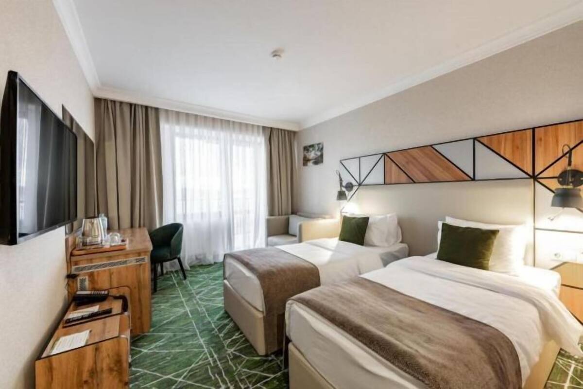 A hotel room with two beds, a desk, a chair, a TV, and a window with curtains.