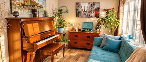 Una sala de estar con un piano de cola, un sofá, un aparador y dos plantas en macetas.