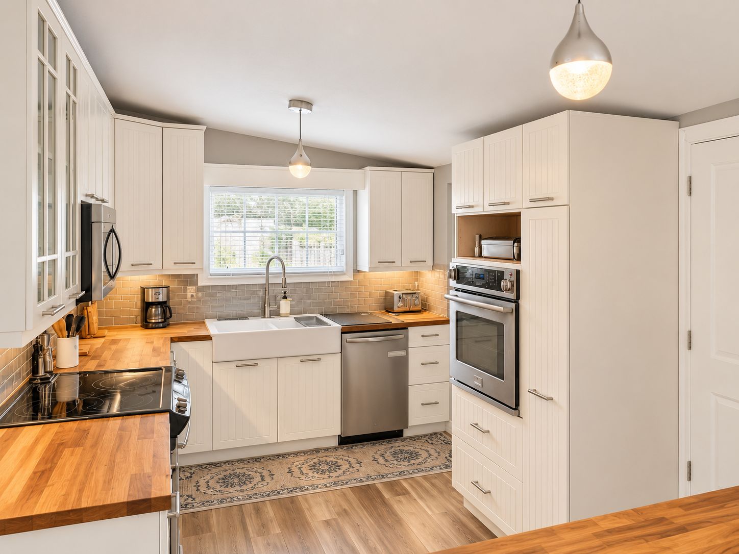 A modern kitchen with white cabinetry, a stainless steel range, a dishwasher, and a window with blinds.
