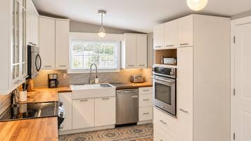 A modern kitchen with white cabinetry, a stainless steel range, a dishwasher, and a window with blinds.