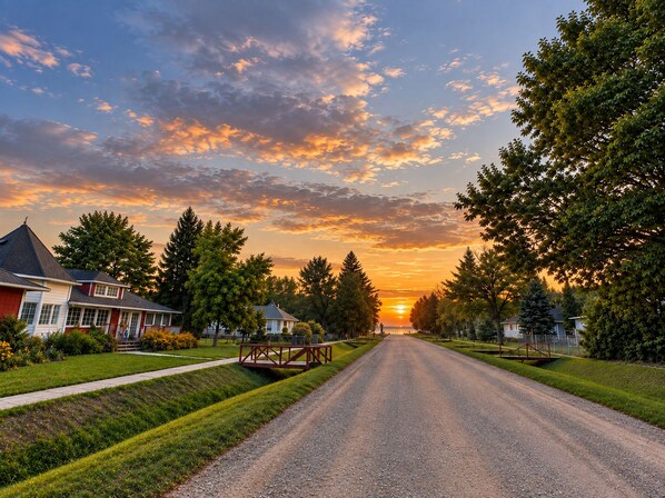 Una calle residencial con casas a ambos lados, cielo despejado y un atardecer.