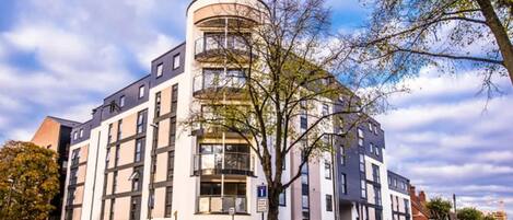 A modern multi-story building with a curved corner, large windows, and a balcony on the upper floor.