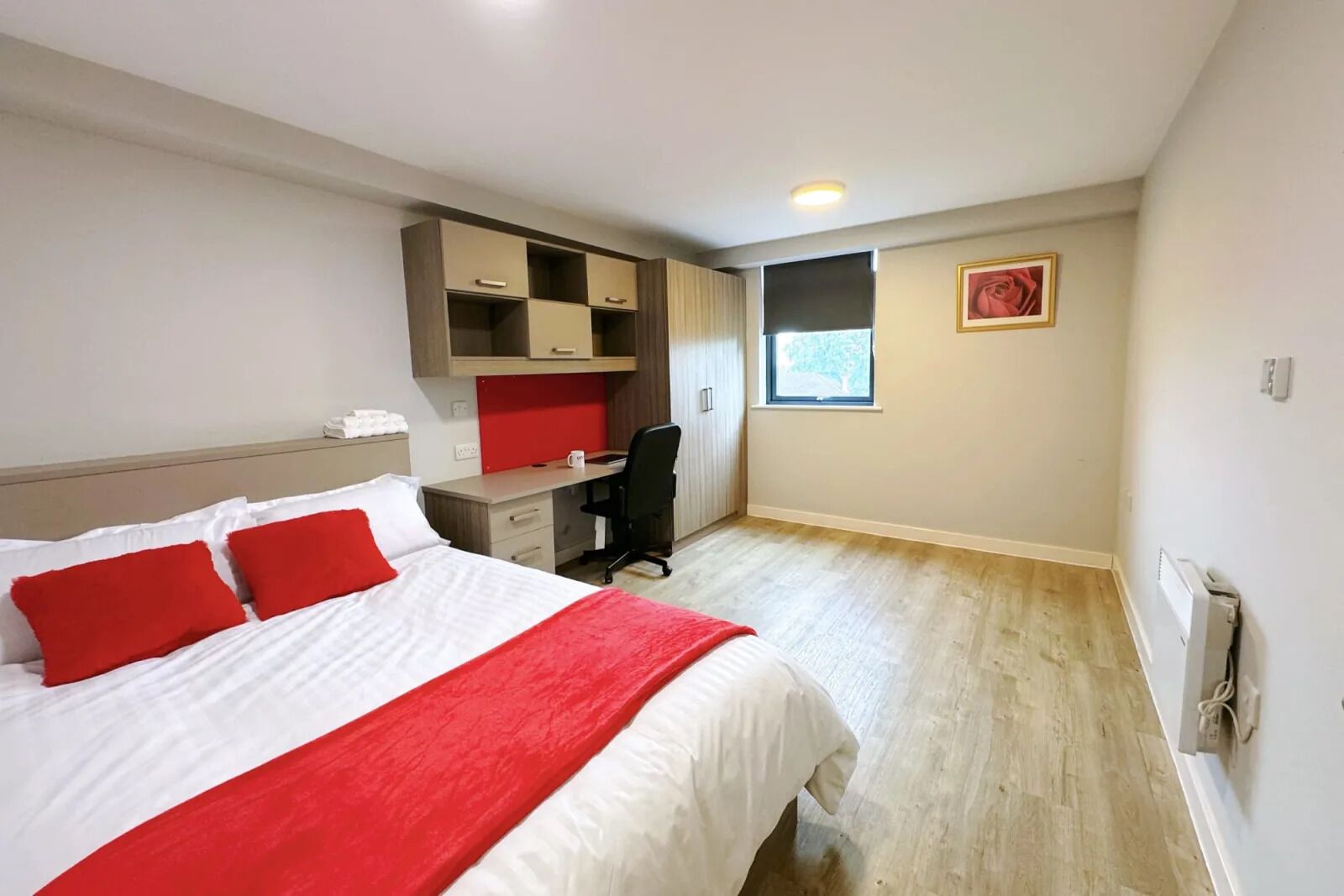 A hotel room with a bed, a desk, a chair, a window, and a radiator.