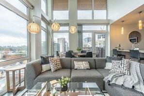 Een moderne woonkamer met een grijze modulaire bank, een glazen salontafel en hanglampen.