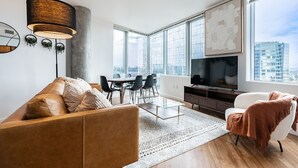 A modern living room with a sofa, coffee table, TV, and dining area. - 2BR | Gym, Pool | Bellevue | Sophari Towers I (Bellevue)