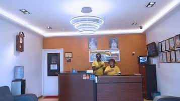 A reception area with a wooden reception desk, two staff members, a water dispenser, and framed pictures on the wall.