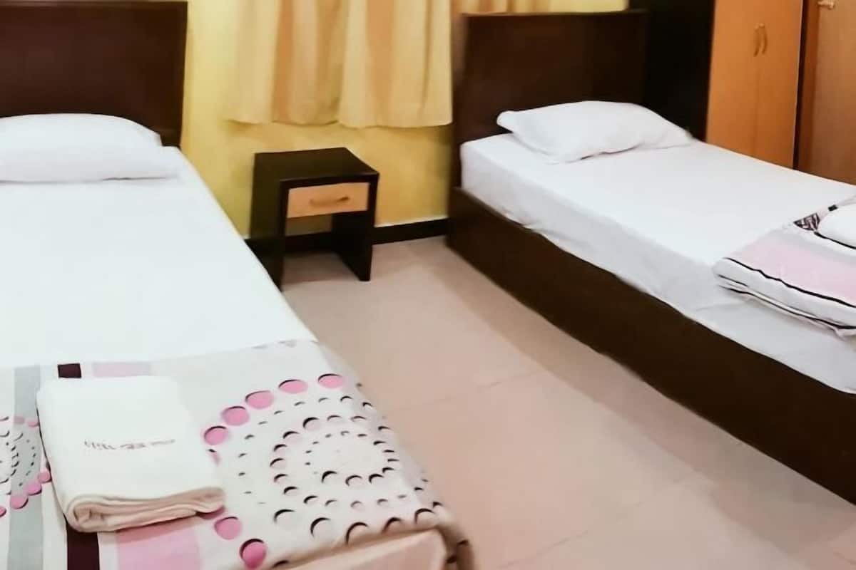 Een hotelkamer met twee eenpersoonsbedden, een klein nachtkastje en een netjes opgemaakt bed met een gevouwen handdoek.