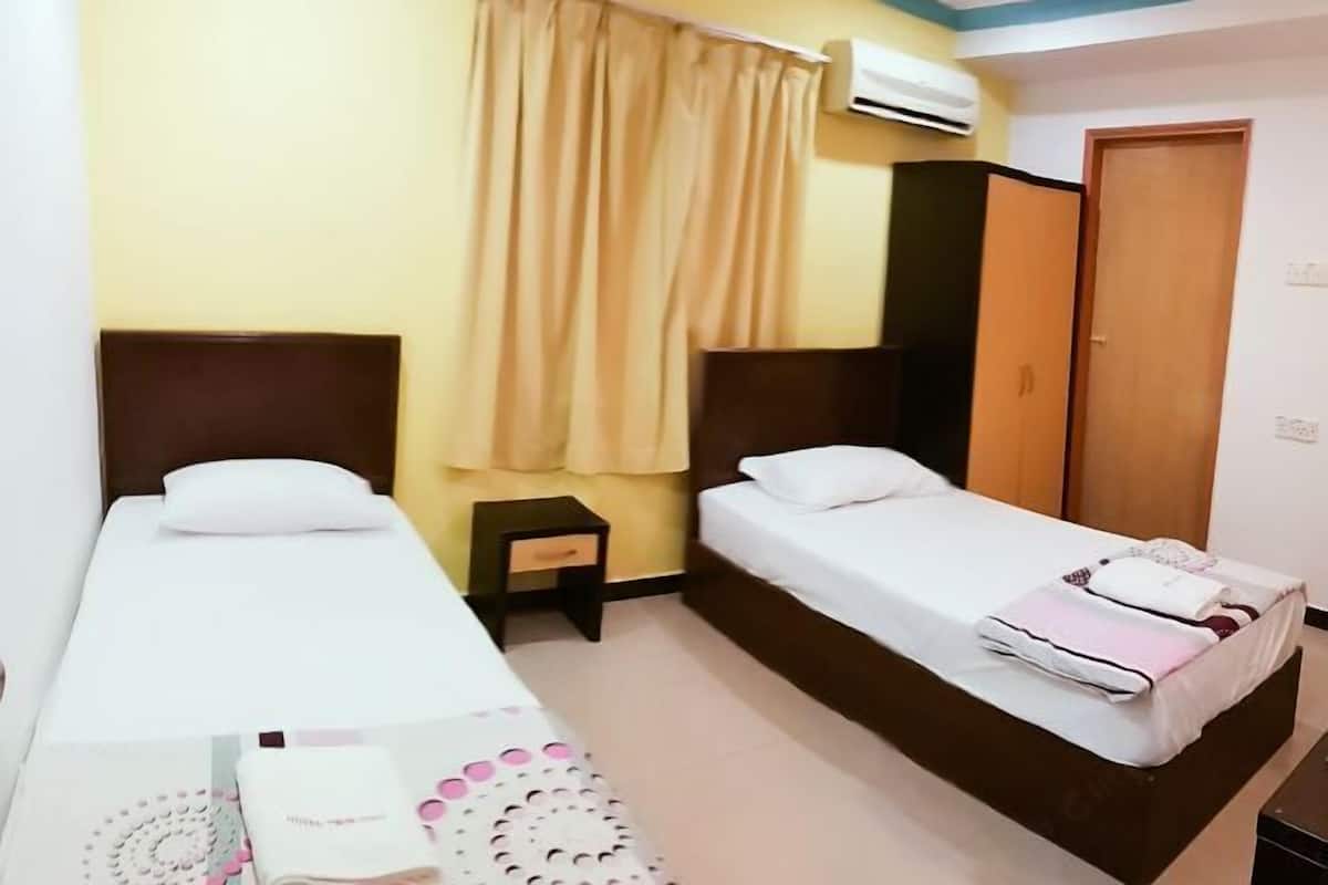 Een hotelkamer met twee enkele bedden, een klein nachtkastje, een kledingkast en een airconditioner aan de muur.