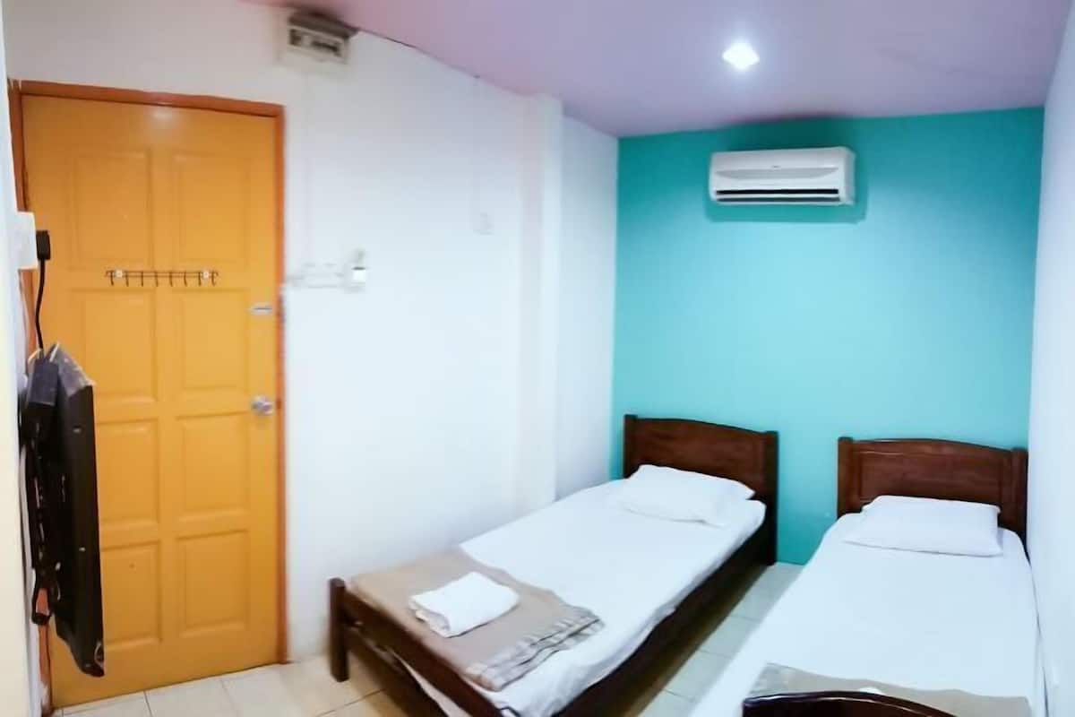 Een kamer met twee eenpersoonsbedden, een houten deur en een airconditioning aan de muur.