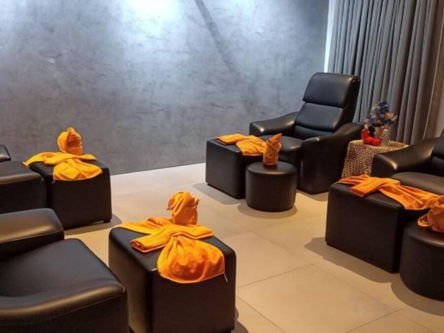 A room with multiple black leather chairs and ottomans, some with orange cloths.