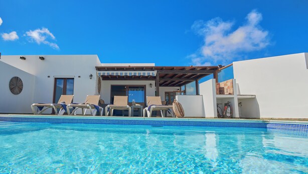 Piscina azul cristalina con sillas de descanso y una zona de estar cubierta.