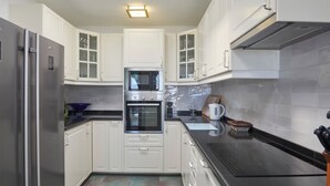 Una cocina moderna con armarios blancos, un refrigerador de acero inoxidable, un horno y un microondas.