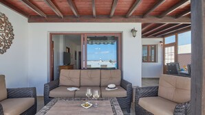 Un área de estar exterior acogedora con mobiliario de mimbre, una mesa con azulejos y vistas al mar.