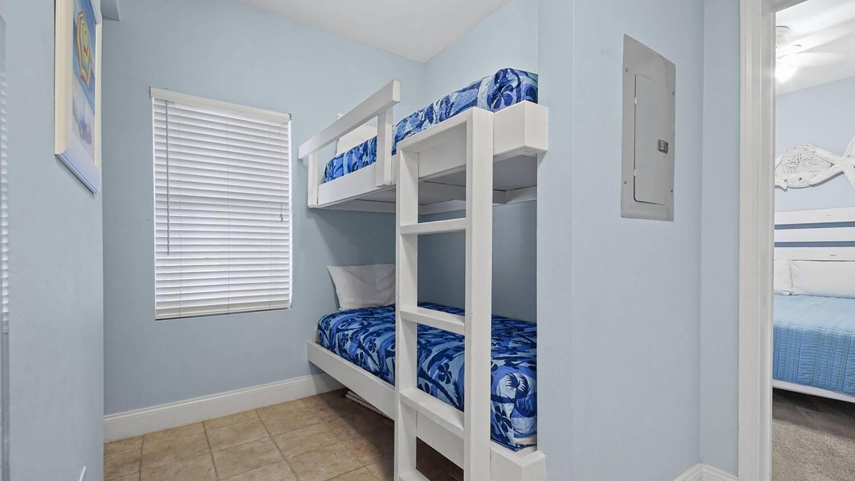 A room with bunk beds, a window with blinds, a door, and a wall-mounted light switch.