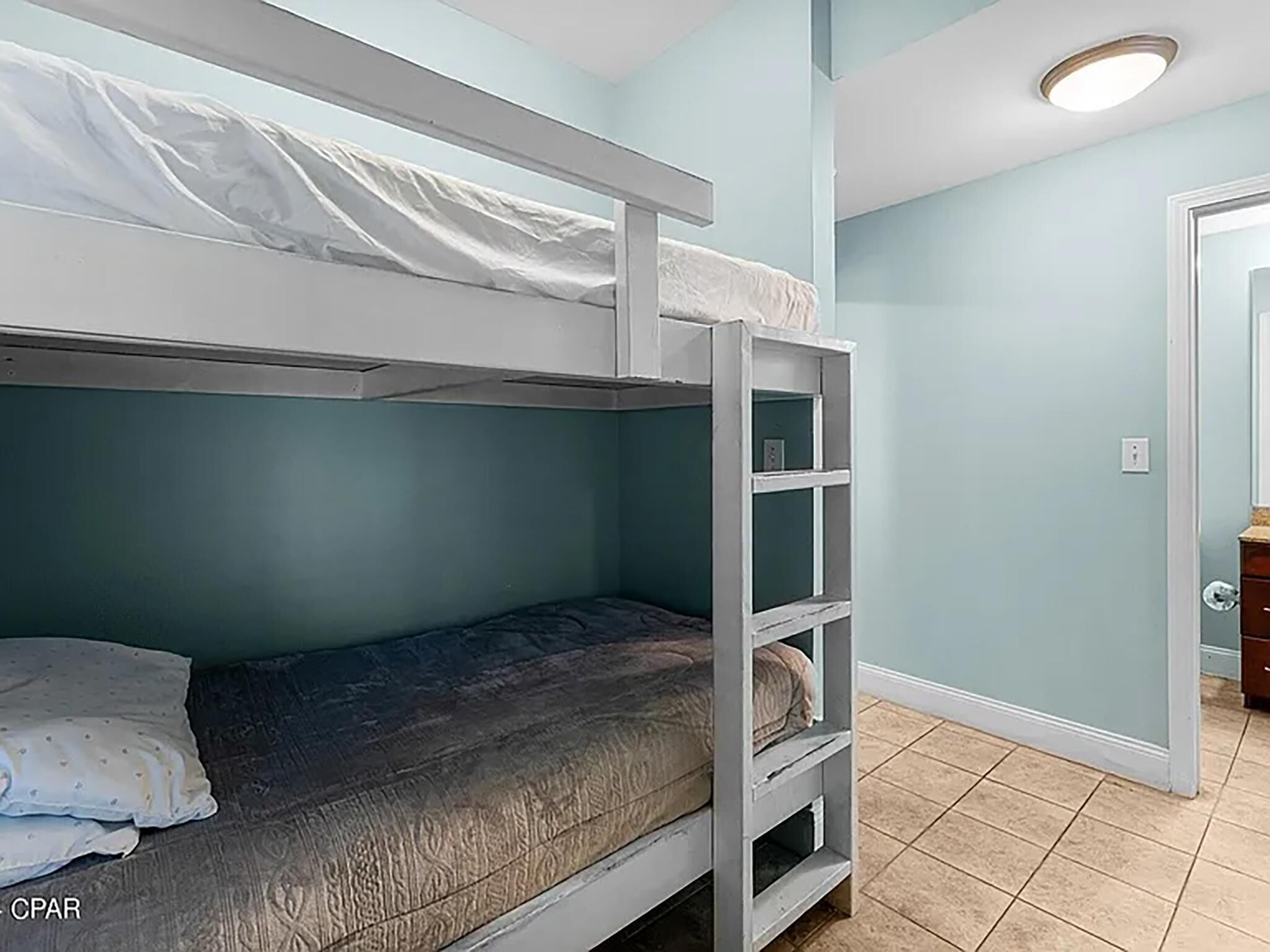 Un lit superposé dans une chambre aux murs de couleur turquoise et au sol carrelé.