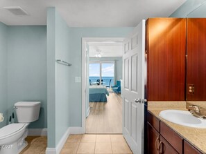 A bathroom with a toilet, a sink, and a view of a balcony with chairs. - Laketown Wharf 1523 (Panama City Beach)