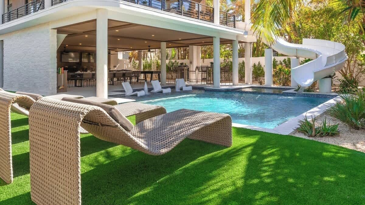 A pool area with lounge chairs, a slide, and a covered seating area with tables and chairs.