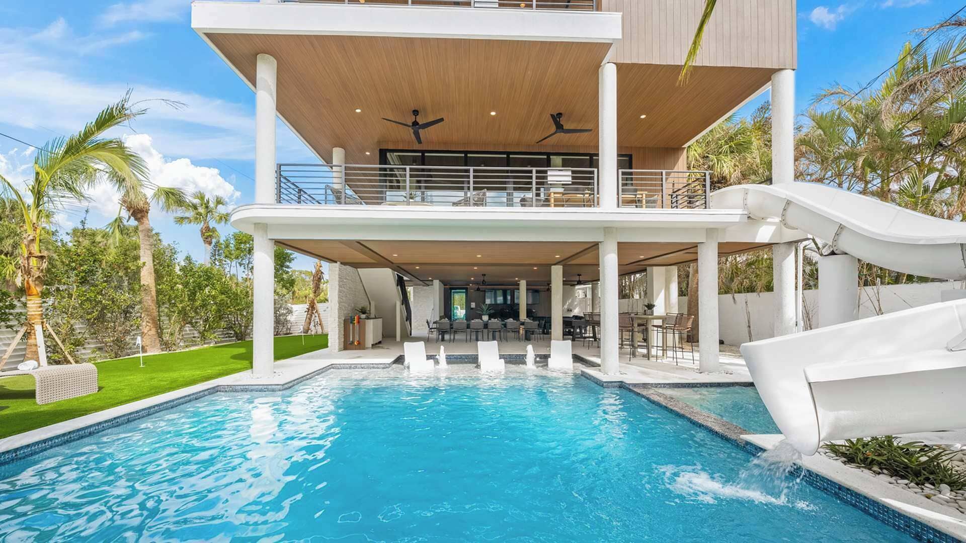 Ein modernes, zweistöckiges Haus mit Swimmingpool, Sitzgelegenheit im Freien und einer Rutsche.