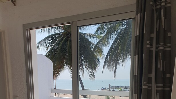 A room with a sliding glass door leading to a balcony with a view of the beach and palm trees.