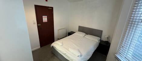 A bedroom with a bed, a nightstand, a red hanging light, a door, and a window with blinds.