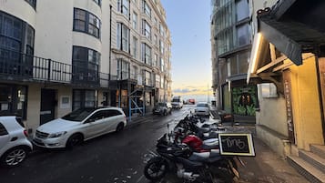 A street with parked cars and motorcycles, buildings with balconies, and a sign for 'Las Vegas Bar'.