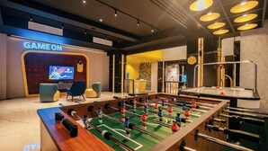A modern indoor game room with a foosball table, a TV screen, and a 'GAME ON' sign. - Yello Hotel Harbour Bay Batam (Batam)