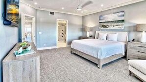 Ein Schlafzimmer mit Bett, Nachttischen, Deckenventilator, einem Gemälde und einer Tür zu einem Badezimmer.