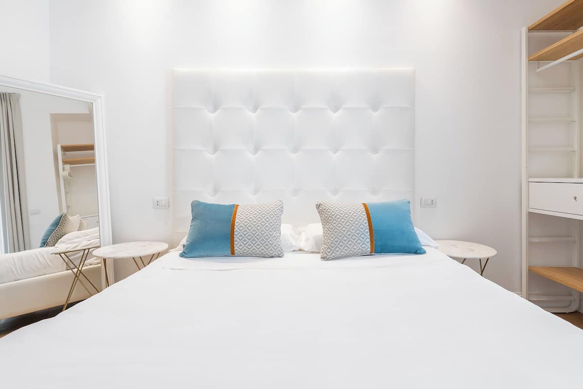 A modern bedroom with a large bed, two bedside tables, a wardrobe, and a mirror.