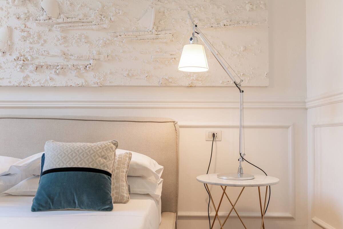 A neatly made bed with pillows, a bedside table with a lamp, and a textured wall.