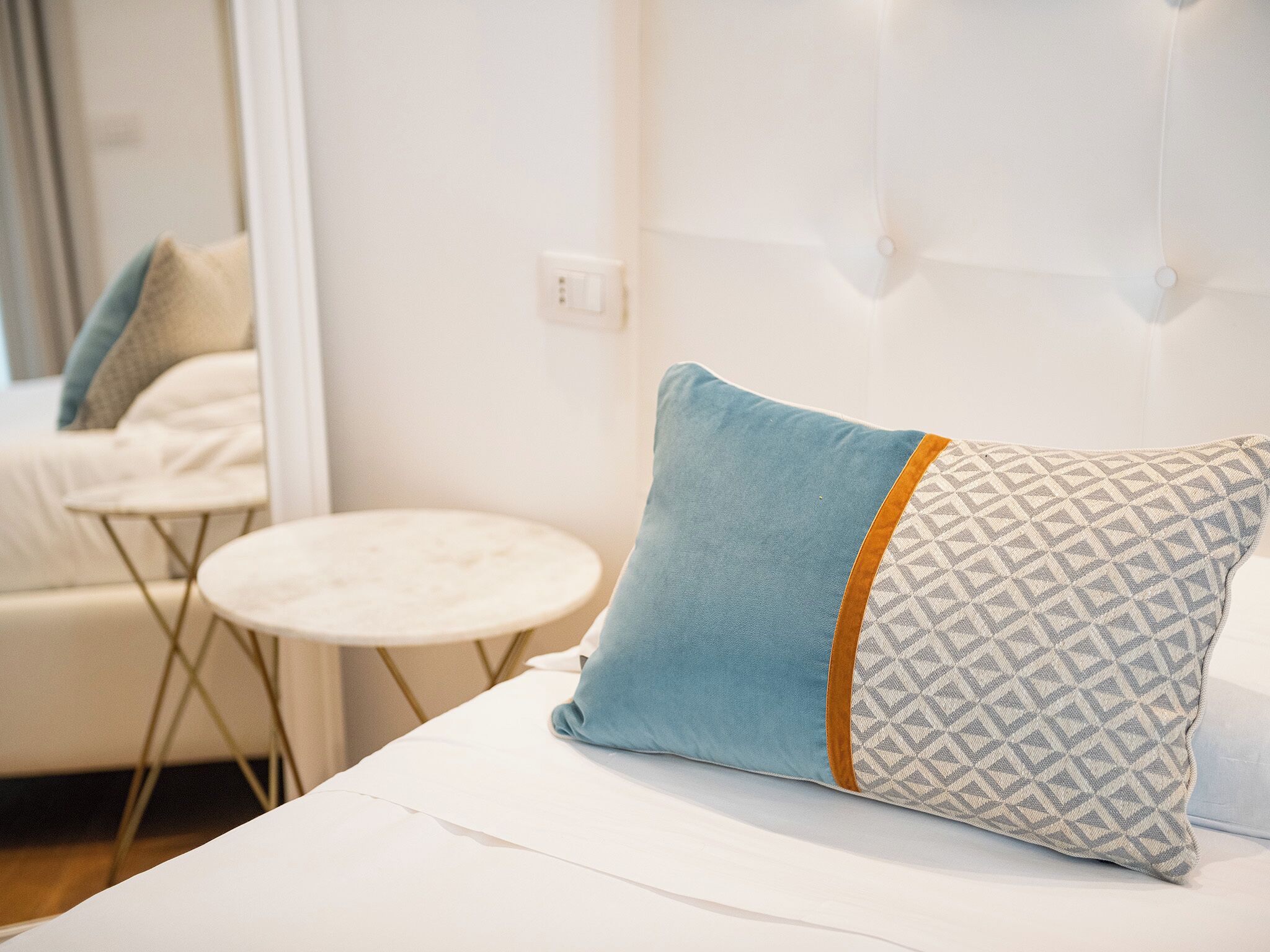 A neatly made bed with a patterned pillow and a small round table beside it.