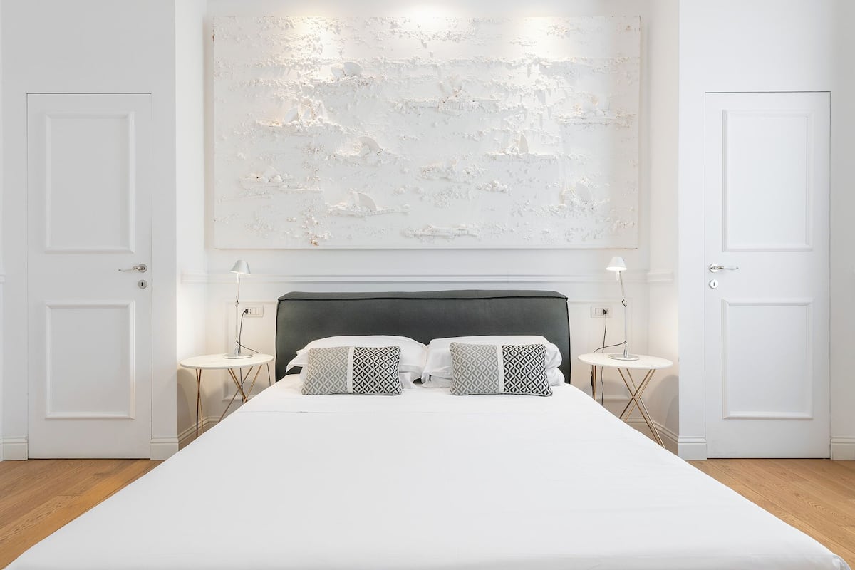 A modern hotel room with a large bed, two bedside tables, and a large abstract painting on the wall.