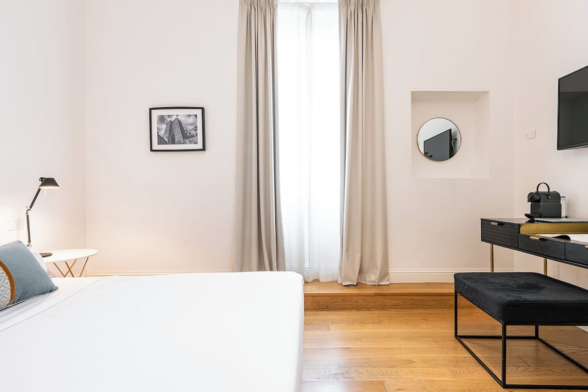 A modern bedroom with a bed, bedside table, lamp, and a desk with a chair.