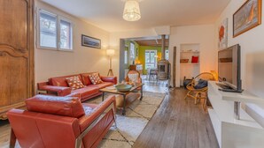 Un salon avec un canapé en cuir rouge, un meuble en bois, un téléviseur et un coin repas comprenant une table et des chaises.