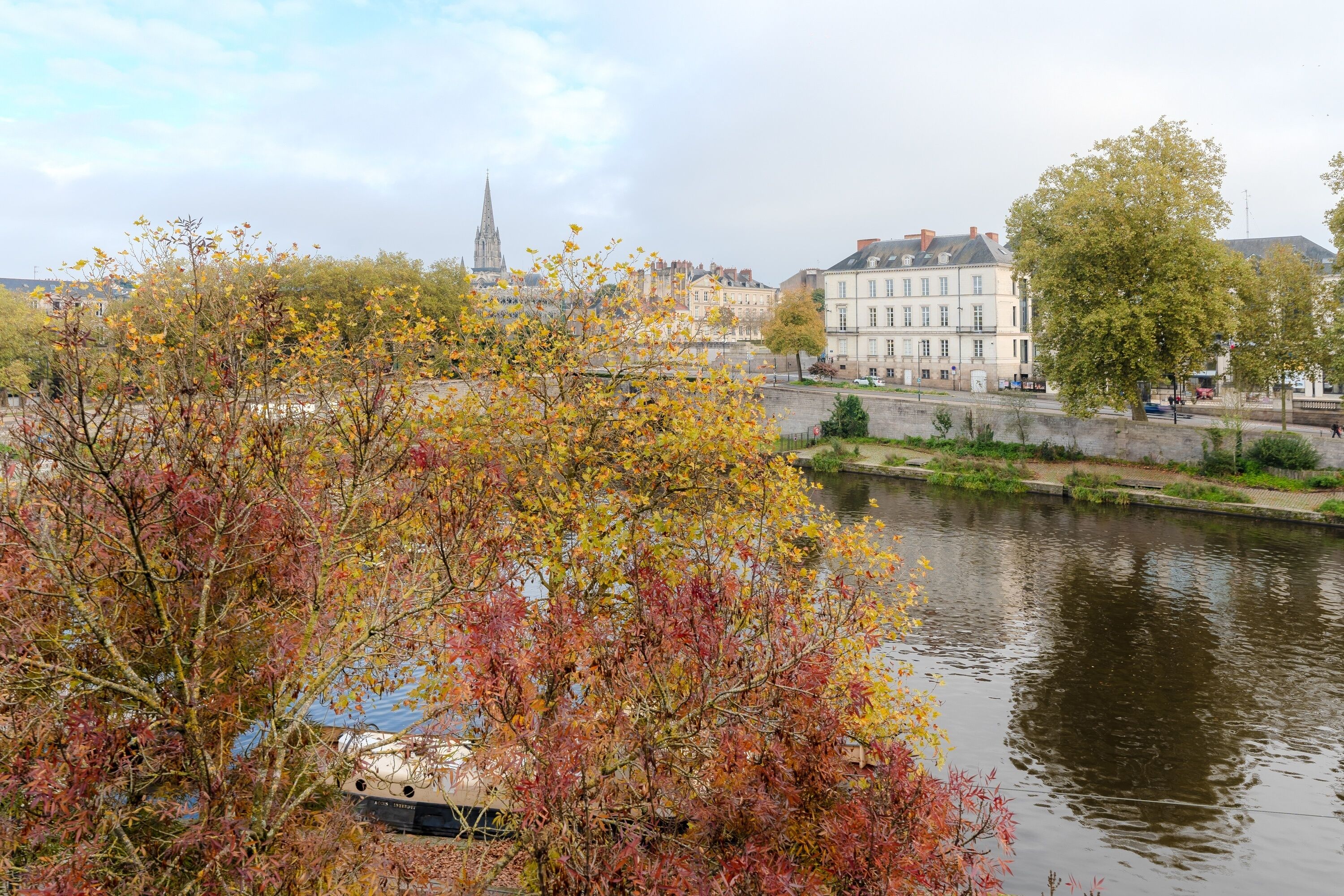 Aussicht auf einen Fluss mit Herbstlaub, historischen Gebäuden und einem Kirchturm im Hintergrund.