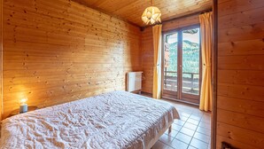 Ein Zimmer in einer Holzhütte mit einem Bett, einer Pendelleuchte und Blick durch eine Glastür nach draußen.