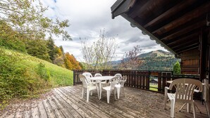 Eine Holzterrasse mit Tisch und Stühlen mit Blick auf eine hügelige Landschaft.